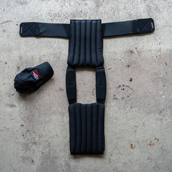 The Achilles | Men's Weighted Vest, featuring padded non-toxic construction, is laid flat on concrete beside a black baseball cap.