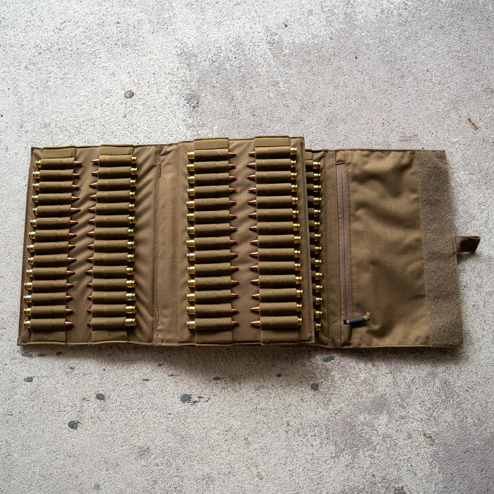 An Ammo Book in tan fabric lies open on a concrete surface, displaying multiple rifle cartridges secured in elastic loops.