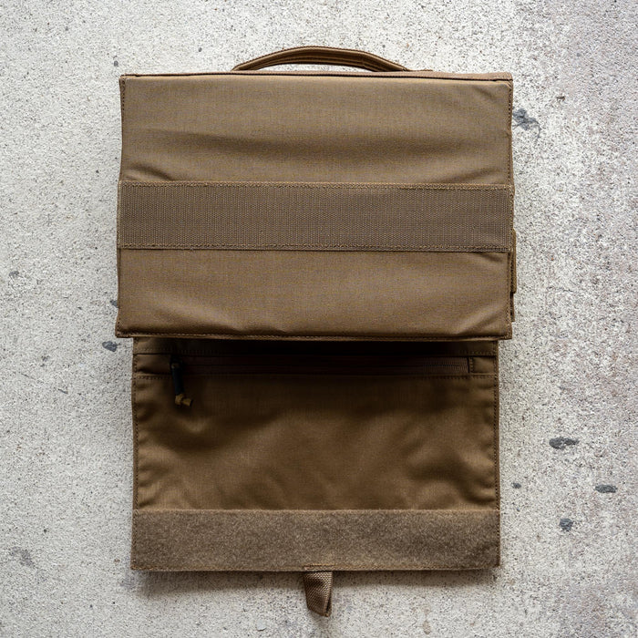 The Ammo Book is a brown fabric bullet organizer pouch with a handle and zippered pocket, shown open on a textured surface.
