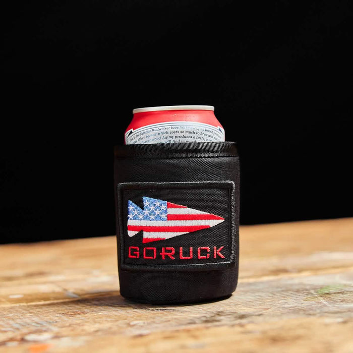 GORUCK black can koozie with American flag patch holding a beverage can on wooden table