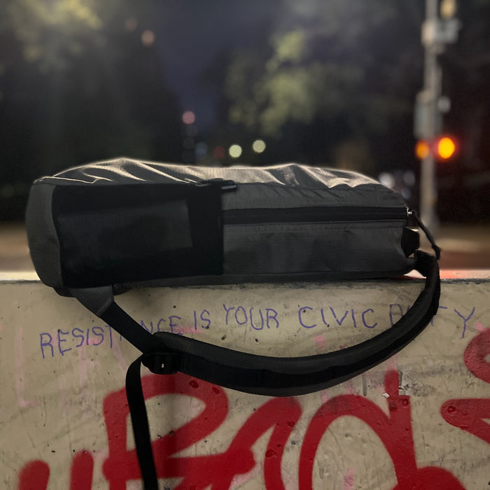 A Basic Rucker rests on a graffiti-covered ledge at night, its gray color highlighted by the glow of blurry street lights in the background—a perfect scene for any GORUCK fan ready to start their rucking journey.
