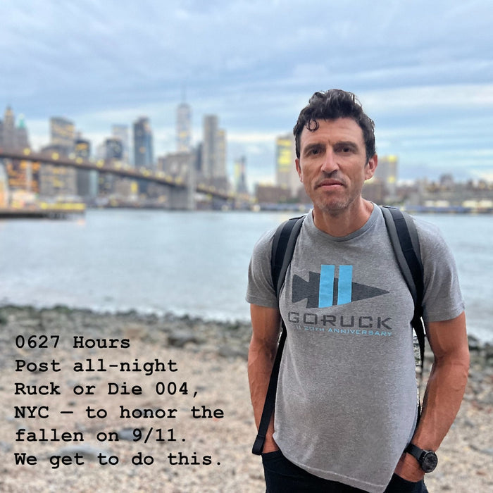 A man stands by the East River with the NYC skyline behind him, wearing a Basic Rucker shirt; event text overlay pays tribute to 9/11 and celebrates the rucking community’s spirit.