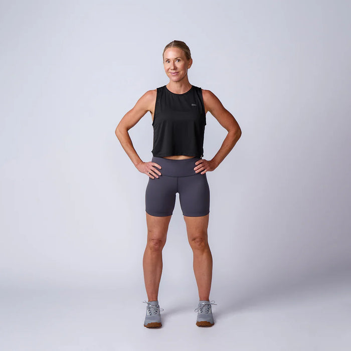 Woman in GORUCK athletic gear, black tank top and gray shorts, standing in studio