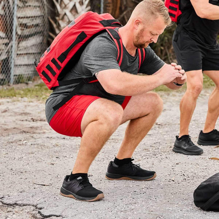 Man performing outdoor squat with red GORUCK rucksack and black training shoes