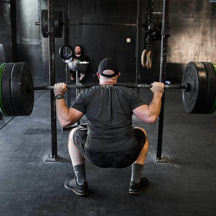 Man performing barbell squat in gym with black GORUCK rucking gear and weight plates