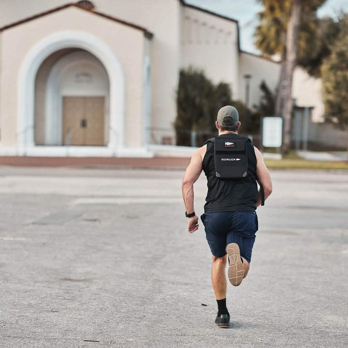 Man running outdoors wearing GORUCK rucksack, black athletic gear, and a cap