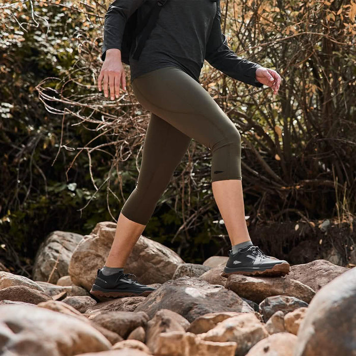 Person hiking over rocks in olive cropped leggings and trail shoes outdoors, GORUCK gear