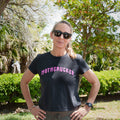 Woman in sunglasses and the GORUCK MOTHERUCKER Women's Tee - Tri-BlendX, featuring a flattering fit, stands outdoors with hands on hips and trees in the background.