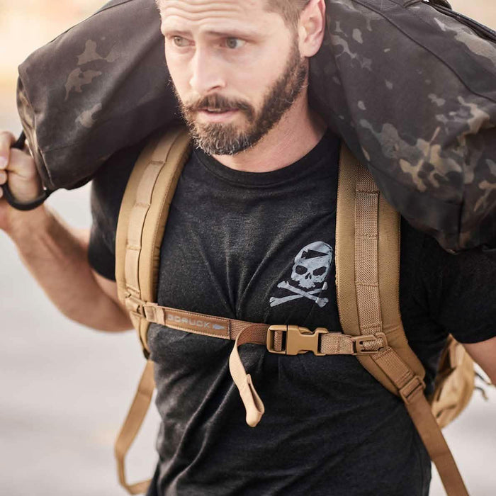 GORUCK athlete wearing black Tribe Tee with skull logo, carrying sandbag and rucking backpack outdoors
