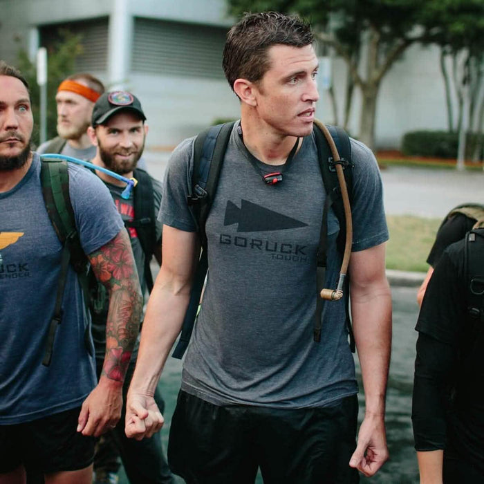 Group of people in GORUCK t-shirts wearing backpacks with hydration hoses outdoors