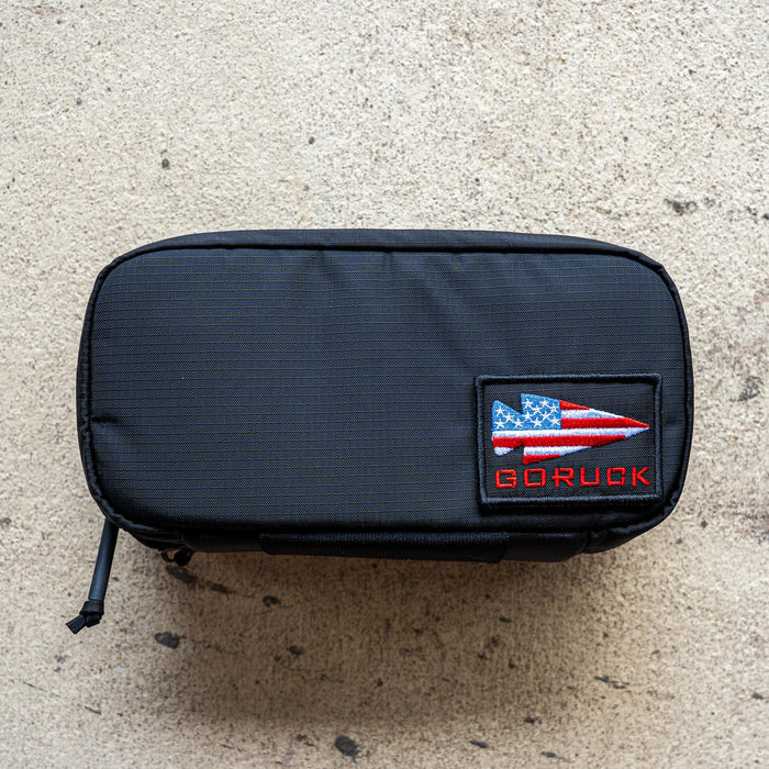 A black IFAK pouch (ROBIC) with red thread, grey interior, and a red patch, featuring an Aquaguard zipper, displayed on a textured surface.