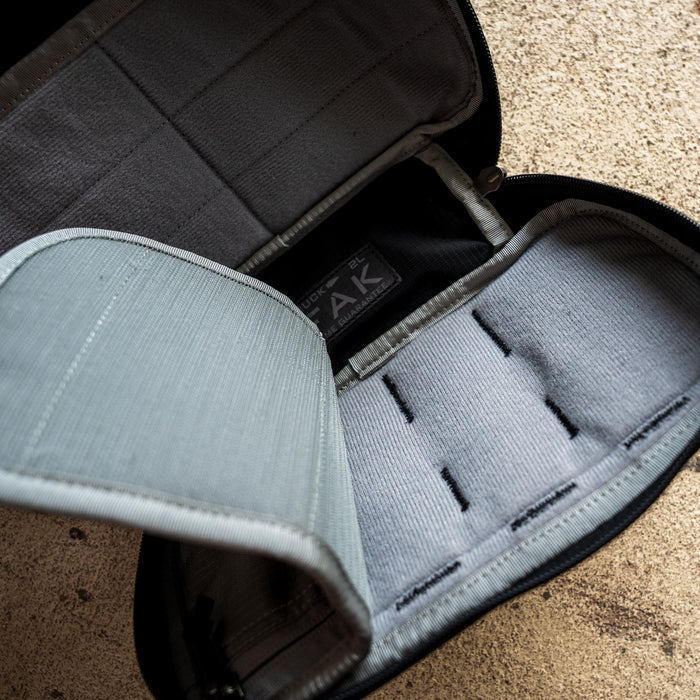 The IFAK (Black + Red Thread + Grey Interior + Red Patch) ROBIC w/ Aquaguard is open, showing its gray interior and velcro straps, lying on a textured beige surface.