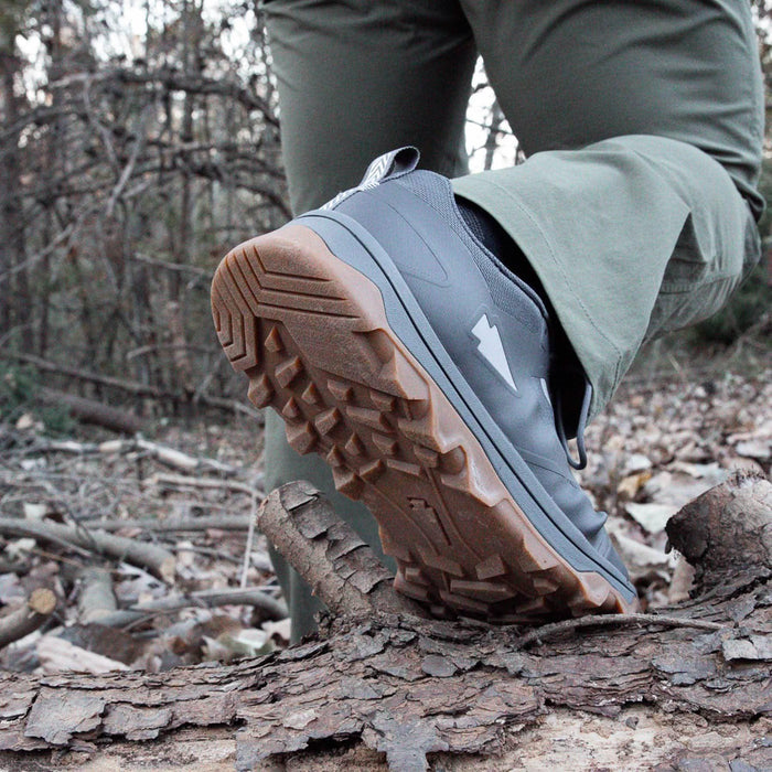 GORUCK trail shoe with rugged sole stepping over log in outdoor forest setting