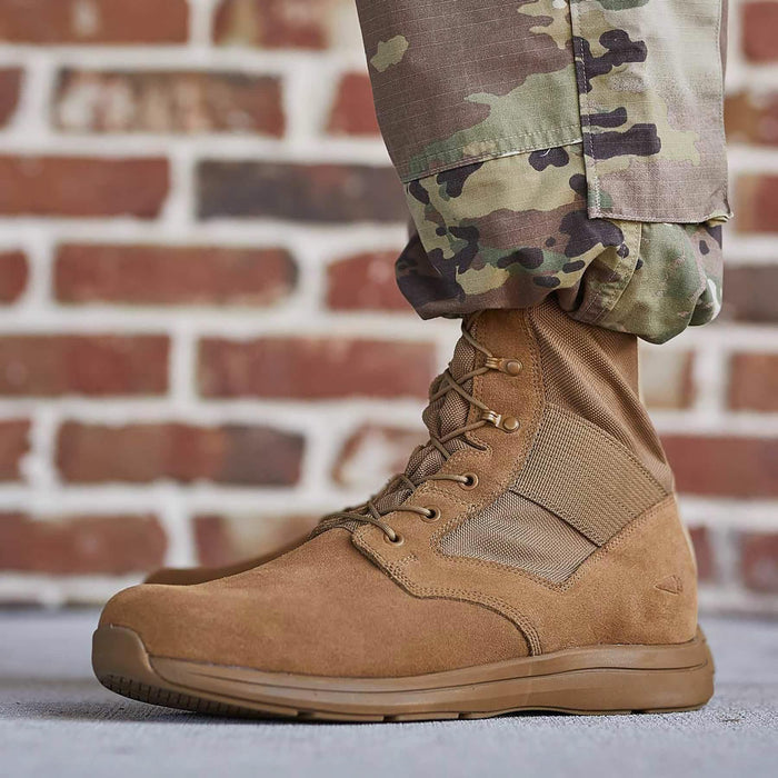 GORUCK brown rucking boot with laces, worn with camouflage pants, brick wall background