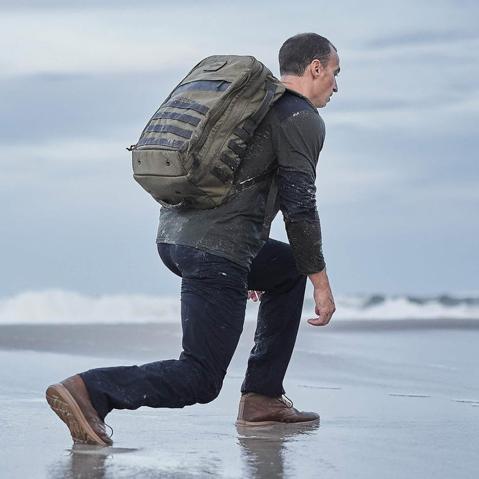Man rucking on wet beach with GORUCK backpack, rugged gear, training by the ocean