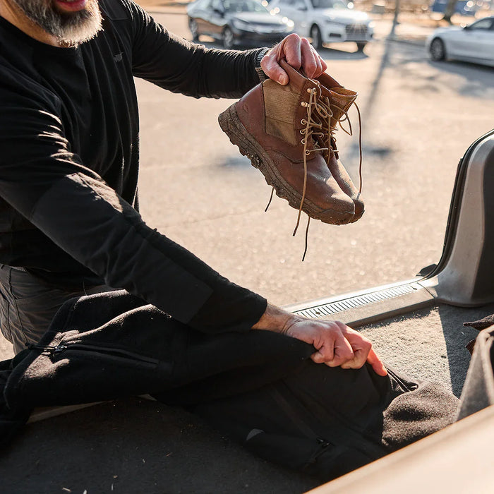 Person packing rugged brown GORUCK MACV-2 boots and black gear bag in car trunk