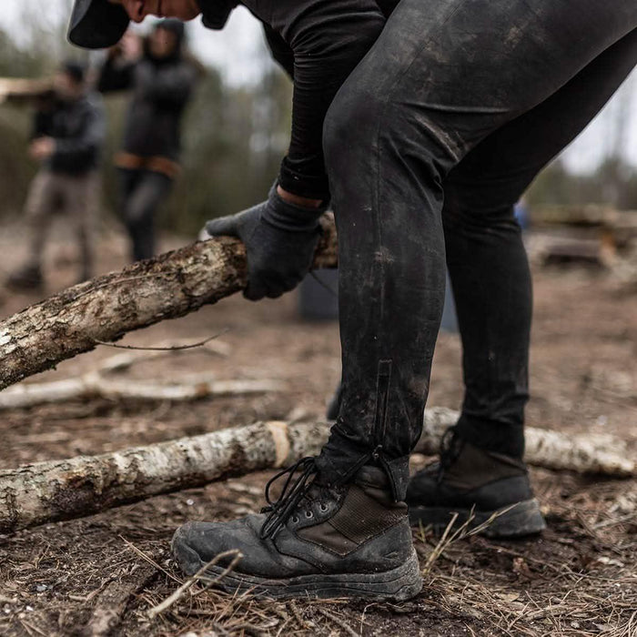 Person in rugged GORUCK boots and gloves lifting a log outdoors during rucking event