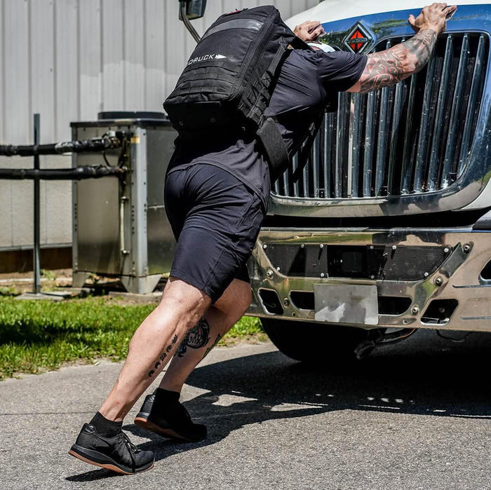 Man wearing GORUCK backpack pushing truck outdoors in rucking workout