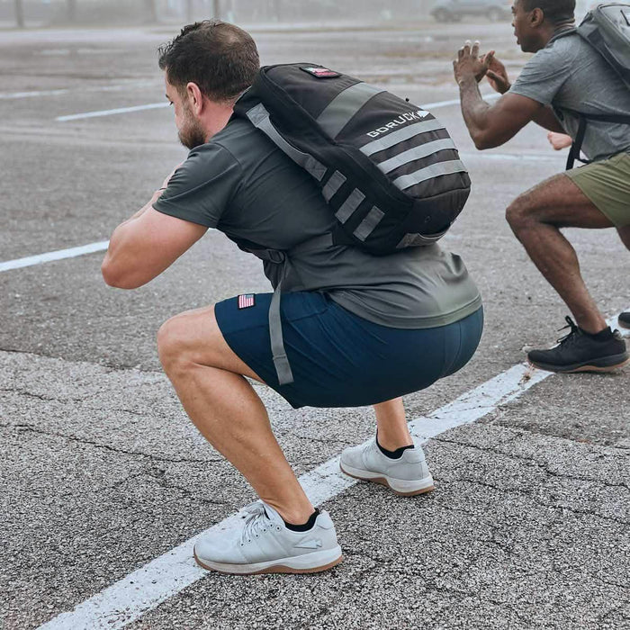 Two men doing squats outdoors wearing GORUCK rucksacks and athletic gear