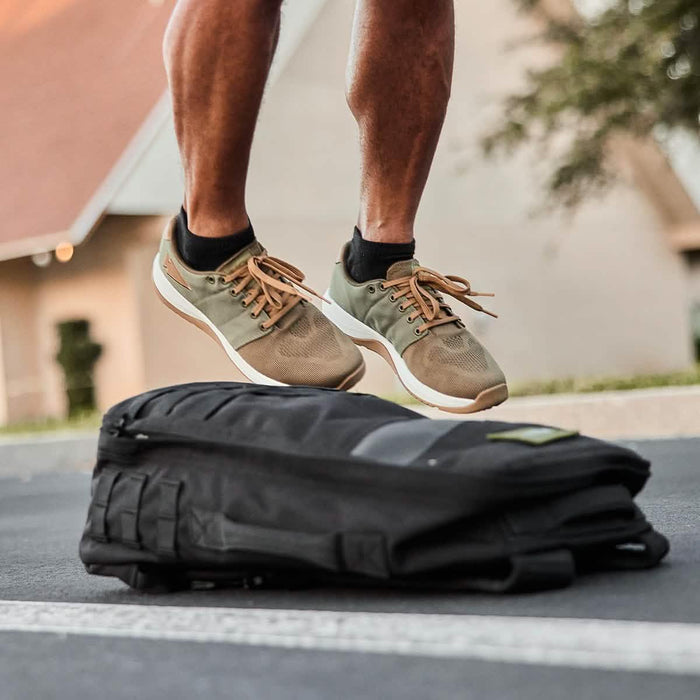 Man wearing GORUCK Ranger shoes jumping over black rucksack outdoors on pavement