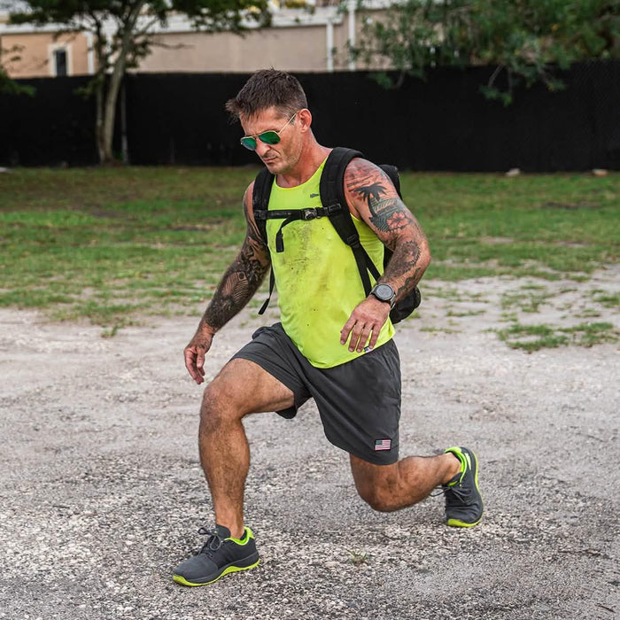 Man in neon tank top and backpack doing outdoor lunge, GORUCK rucking workout gear