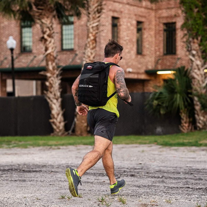 Man rucking outdoors with GORUCK backpack, athletic gear, palm trees and brick building in background