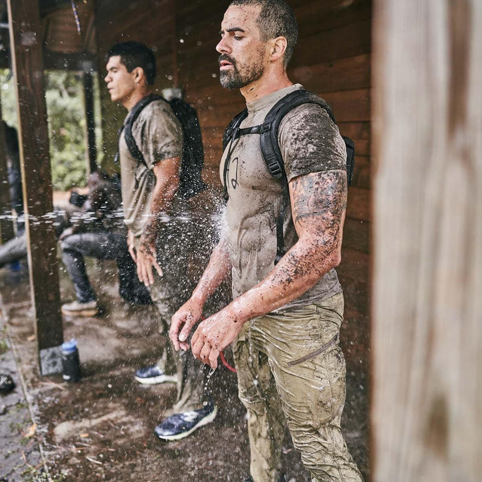 Two men in GORUCK pants and backpacks rinse off mud during outdoor rucking training.