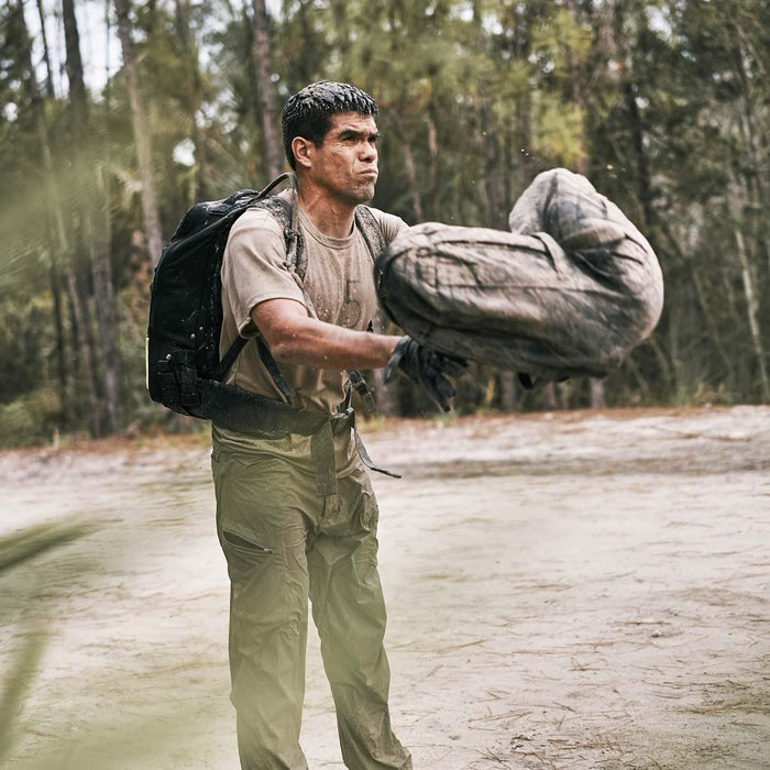 Man in GORUCK pants and backpack tossing a sandbag outdoors during rucking workout