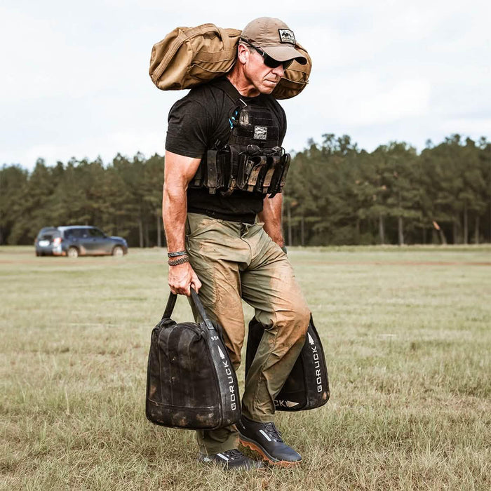 Man wearing GORUCK Challenge Pants in ranger green, rucking with weighted bags outdoors