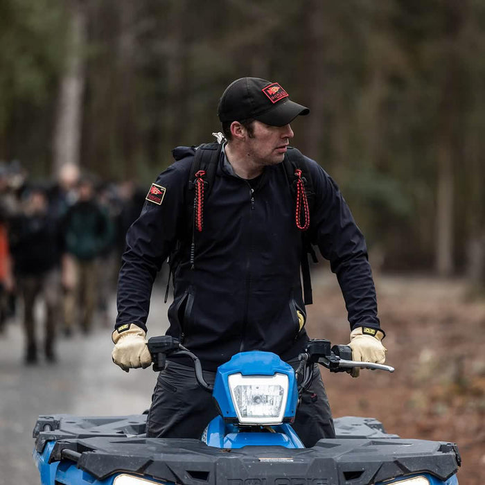 GORUCK team member in black gear and hat on blue ATV during outdoor rucking event