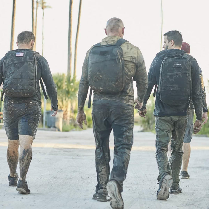 Group of people in muddy clothes wearing GORUCK backpacks during outdoor rucking event