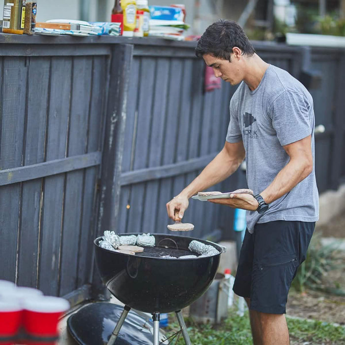 Man in GORUCK t-shirt grilling burgers outdoors at backyard barbecue event