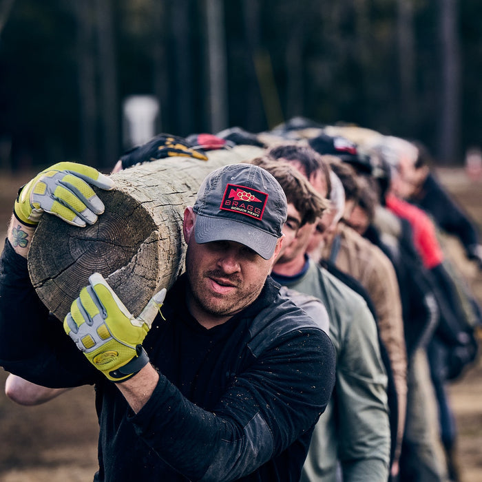 A group of people, wearing Men’s Commando Pullover - Merino Wool, carries a large log together on their shoulders during an outdoor team activity.