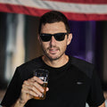 A man in sunglasses and the Men’s Commando Tee - Merino Wool with reinforced shoulders holds a beer, standing before an American flag.
