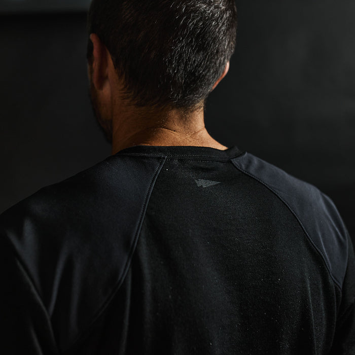 Close-up of a man’s back wearing the Men’s Commando Tee - Merino Wool in black, featuring reinforced shoulders. His short dark hair stands out against the dark background.