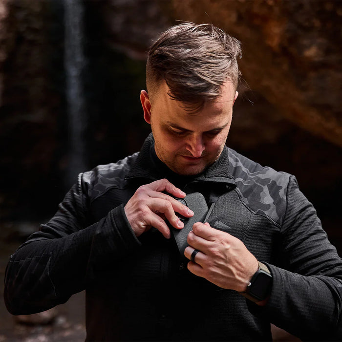 Man wearing GORUCK black camo grid fleece half-zip jacket outdoors, unzipping chest pocket