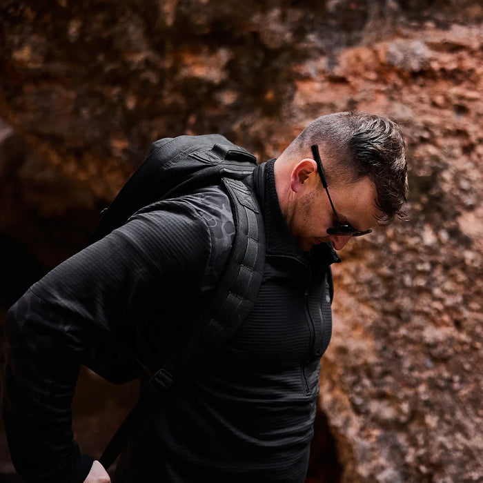 Man wearing black GORUCK Grid Fleece half-zip and rucksack outdoors near rocks