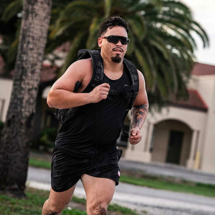 Man running outdoors in GORUCK black performance tank and ruck backpack, palm trees behind