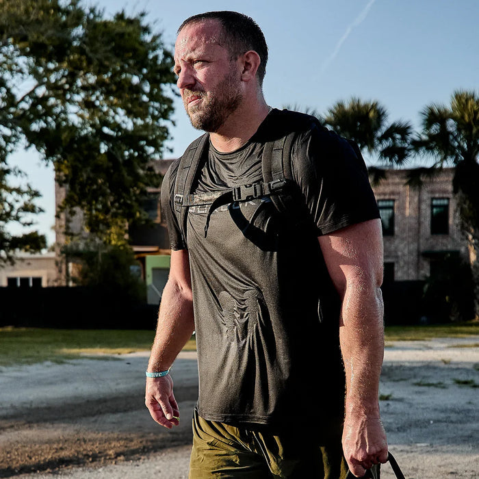 Man outdoors wearing GORUCK black performance tee and backpack, rucking in the sun