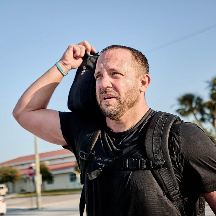 Man wearing GORUCK Tough Mesh Tee and backpack outdoors, carrying rucking gear.