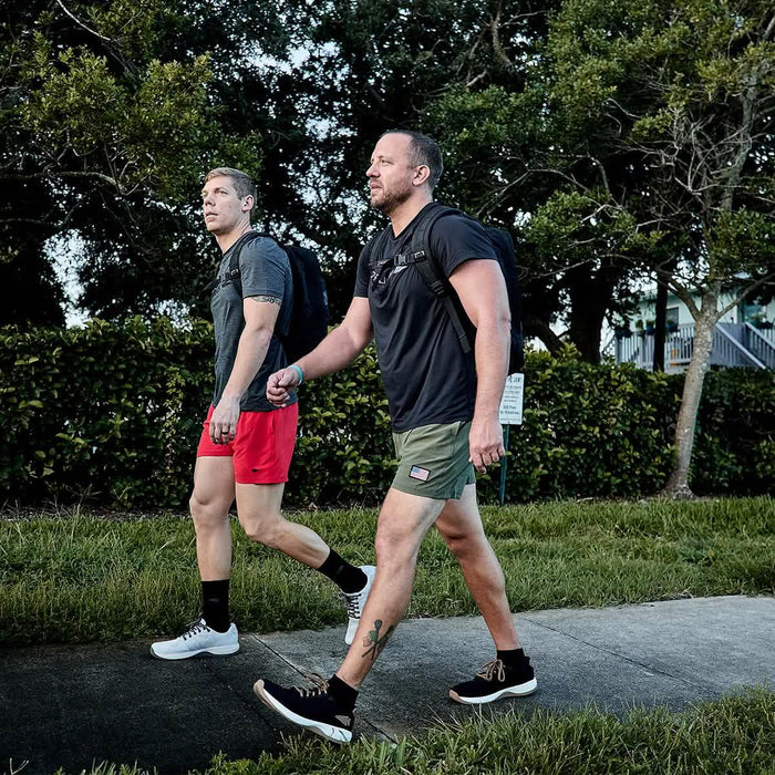 Two men rucking outdoors wearing GORUCK gear, black Tough Mesh Tee, shorts, and backpacks