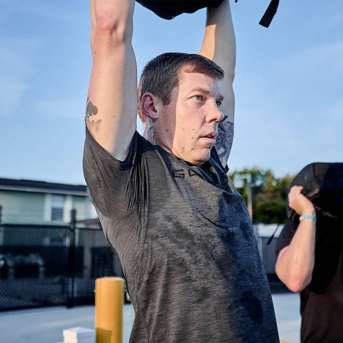 Man lifting weighted ruck over head outdoors in GORUCK workout gear