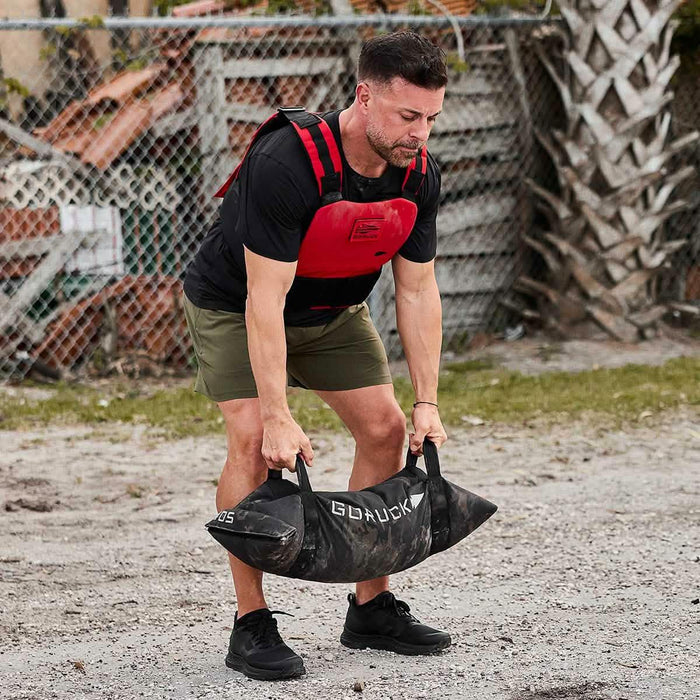 Man wearing GORUCK gear lifting sandbag outdoors, showcasing rucking fitness equipment