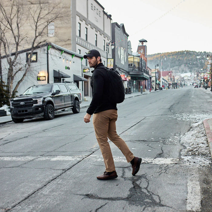 Man wearing GORUCK backpack crossing urban street in casual outdoor gear