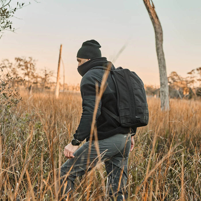 Man rucking outdoors in field at sunset wearing GORUCK backpack, beanie, and jacket
