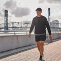 Man rucking in GORUCK long sleeve performance tee by riverfront, bridge in background