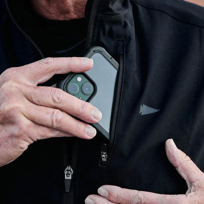 Man placing a smartphone into a GORUCK jacket chest zipper pocket, durable outdoor gear