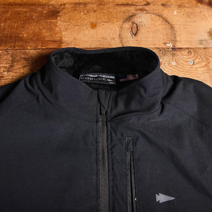 GORUCK black rucking jacket with zipper and arrowhead logo on wooden background