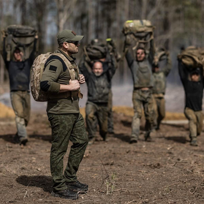 Group of people outdoors in camo gear carrying heavy backpacks, GORUCK rucking event training