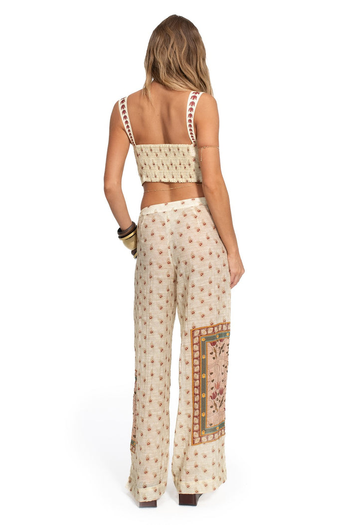 Beige crop top with decorative straps, paired with wide-leg pants in matching small pattern detail print and ornamental panel detail